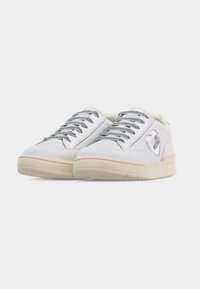 Λευκά sneakers χαμηλού πάνω μέρους με ασημένιες κορδέλες και μπεζ σόλες, με ένα λογότυπο σε σχήμα καρδιάς στη πλευρά που γράφει "LOVE MOSCHINO".