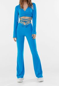 Blue two-piece outfit featuring a long-sleeve wrap top with cut-outs and matching flared pants. Smooth fabric with a fitted design.