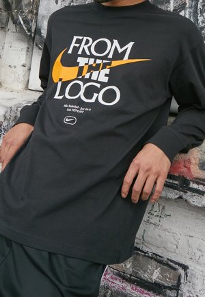 Czarna bluzka z długim rękawem z pomarańczowym i białym napisem "FROM THE LOGO" oraz logo Swoosh Nike, wykonana z miękkiego materiału bawełnianego.
