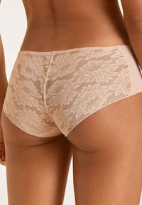 Nude lace slipje met bloemmotieven; zachte, semi-doorzichtige kantoverlay op de achterkant, gladde stof aan de voorkant voor comfort en pasvorm.