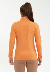 Langarmige, oranje sporttop met hoge kraag, gladde textuur en aansluitend ontwerp, met een naad over de bovenrug.