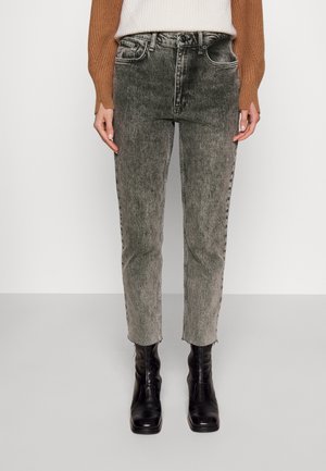 Person iført grå acid-vaskede jeans, sorte ankelstøvler, en hvid ribbet sweater og en brun langærmet cardigan.