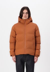 Puffervest i rustorange med hætte, fuld lynlås og polstret design. Bæres med mørke denimbukser.