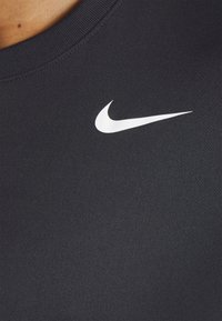 Camiseta deportiva negra hecha de una tela suave, con el logo blanco de Nike en el área del pecho izquierdo. Cuello redondo con textura acanalada.