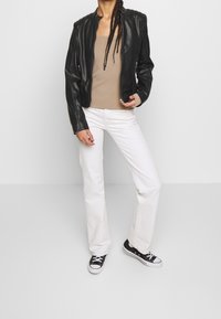 Schwarze Lederjacke mit gestepptem Schulterdetail, beiges Tanktop, weiße Schlagjeans und schwarze Sneakers mit weißen Sohlen.