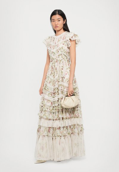 Maxi-jurk met bloemenpatroon in wit en pasteltinten, met rimpels aan de mouwen en gelaagde tule textuur; model houdt een crèmekleurige clutch bij zich.