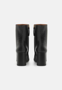 Botas de cuero negro hasta el tobillo con punta cuadrada y tacón cuadrado. Presentan una cremallera dorada y una superficie texturizada. El interior es de color marrón.