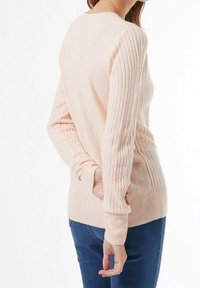 Roze gebreide trui met gestructureerde ribben mouwen, ronde hals en lange mouwen, gecombineerd met blauwe jeans, gezien vanaf de achterkant.