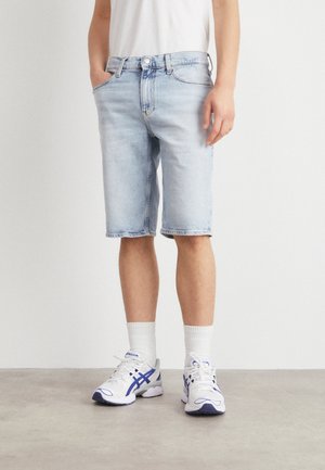 Pantalones cortos de mezclilla azul claros con cinco bolsillos y corte recto. Combinados con zapatillas blancas y calcetines blancos hasta el tobillo.