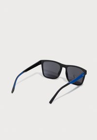 Ochelari de soare negri cu lentile întunecate. Bratele au o dungă albastră și un mic accent cu logo. Design clasic cu ramă dreptunghiulară.