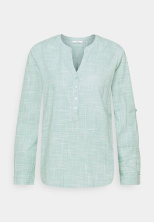 Chemise à manches longues vert clair avec un motif de grille texturé, décolleté en V et patte de boutonnage à trois boutons. Dispose de languettes pour retrousser les manches.