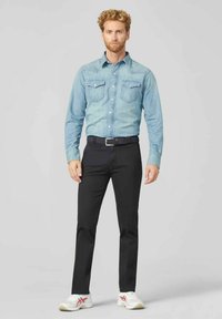 Helles, blaugraues Denimhemd mit zwei Brusttaschen, schwarze Hosen und weiße Sneakers mit roten und blauen Akzenten. Einfaches, schmal geschnittenes Design.
