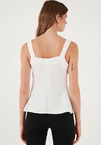 Fehér ujjatlan felső négyzet alakú hátrésszel, széles pántokkal és bővülő aljjal. Sima textúra és letisztult dizájn, rétegezéshez ideális.