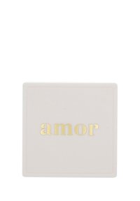 Vitt fyrkantigt föremål med guld präglat ordet "amor" centrerat på ytan, placerat mot en enfärgad vit bakgrund.