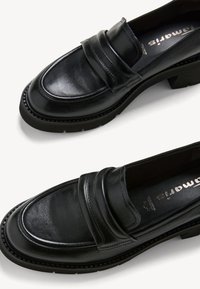 Mocassins en cuir noir avec un bout arrondi, double sangle décorative, semelle épaisse et texturée, et talon légèrement surélevé. Fini lisse avec un éclat subtil.