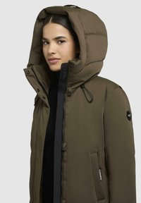 Olivgrüne Pufferjacke mit großer Kapuze, Reiß- und Druckknopfverschlüssen, verstellbarem Kordelzug und Seitentaschen. Glattes Nylonmaterial mit dezentem Glanz.