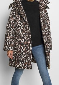 Manteau matelassé avec un imprimé animalier marron, blanc et noir, col montant, fermeture éclair et deux grandes poches latérales.