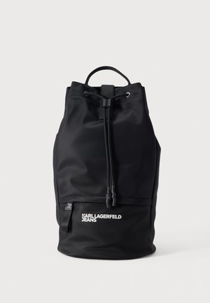 Sac à dos noir Karl Lagerfeld Jeans à cordon de serrage, avec une poignée supérieure, une poche avant zippée et un logo blanc, présenté sur un fond clair.