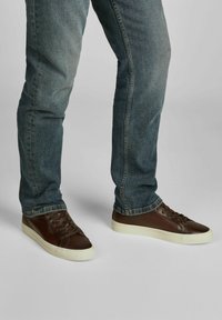 Bruine leren sneakers met een gladde textuur, witte rubberen zool en platte veters, gecombineerd met blauwe spijkerbroeken.