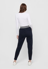 Mornarska trenerka s uskim krojem i elastičnom waistband trakom s bijelim prugama. Uparena s dugim bijelim topom. Minimalistički dizajn.