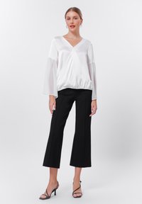 Blouse en satin blanc avec un col en V, des manches évasées et un ourlet froncé, accompagnée d'un pantalon large noir et de talons noirs à brides.