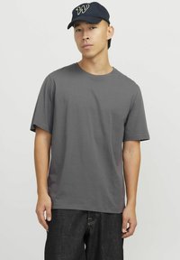 Camiseta de algodón de manga corta gris, con un clásico cuello redondo y un corte holgado. Combinada con jeans oscuros y una gorra azul marino.