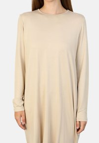 Robe beige à manches longues avec un col rond, texture douce et coupe décontractée, arborant un design simple sans motifs ni embellissements.