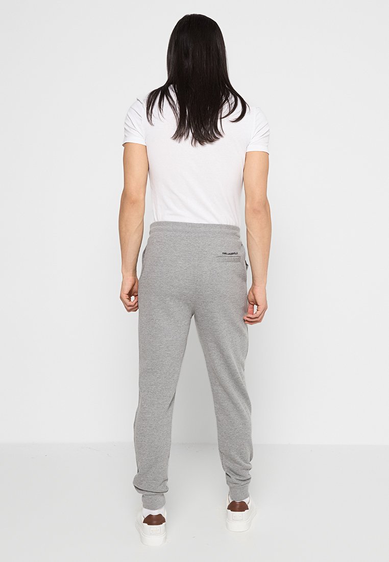 Pantalones de chándal grises con cintura elástica, que cuentan con un bolsillo trasero, combinados con una camiseta blanca y zapatillas blancas.