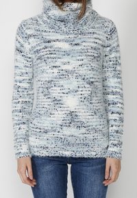 Pull en tricot bleu clair, texturé, avec un col roulé, arborant un design moucheté de bleu foncé et de blanc, avec des manches longues et une coupe décontractée.