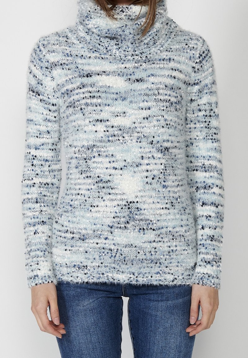 Pull en tricot bleu clair, texturé, avec un col roulé, arborant un design moucheté de bleu foncé et de blanc, avec des manches longues et une coupe décontractée.