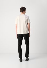 Cream cotton t-shirt with short sleeves, paired with black trousers. The t-shirt features a simple, clean design, emphasizing comfort and fit.