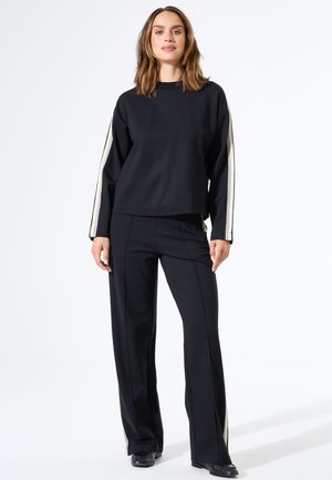 Schwarzer, taillierter Sweatshirt mit langen Ärmeln, der cremefarbene Seitenstreifen hat, kombiniert mit maßgeschneiderter schwarzer Hose mit seitlichen Streifendetails.