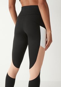 Høj talje leggings med en sort hoveddel og hvide samt hudfarvede udskæringer, der fremhæver et glat, strækbart stof og et elegant design.