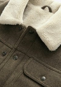 Braune Wollmischung Jacke mit einem cremefarbenen Faux-Schafslederkragen, ausgestattet mit schwarzen Metall-Druckknöpfen und einem Brusttaschen-Detail.