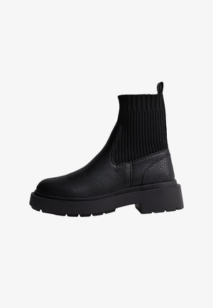 Mustat nilkkurit, joissa on teksturoitu nahkapinta ja ribbaattikangaspanta. Paksu kumipohja kestävyyttä ja lisäkorkeutta varten.