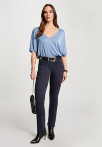  Lichtblauw, kortemouwen V-hals top van een glanzende stof, gecombineerd met donkere, strakke jeans, een zwarte riem en hoge zwarte laarzen.