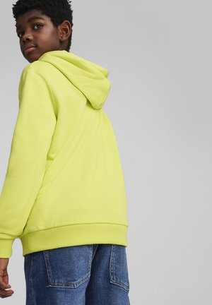 Sudadera amarilla brillante con capucha, puños acanalados y dobladillo. Combinada con pantalones de mezclilla azules que presentan grandes bolsillos. Textura suave.
