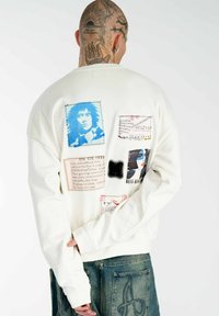 Weißer Sweatshirt mit verschiedenen Stoffpatches und blauen, schwarzen und roten Grafiken; enthält Text und unterschiedliche Texturen auf der Rückseite.