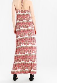 Robe maxi avec un motif en rose et rouge sur fond blanc. Fabrication en tissu léger, elle présente un col halter et une coupe fluide.