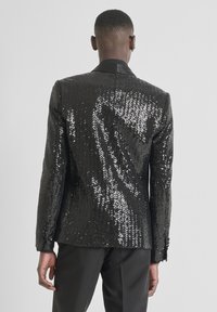 Blazer negro con lentejuelas y superficie texturizada, con cuello de satén y detalles de botones, diseñado con un ajuste entallado y una silueta definida.