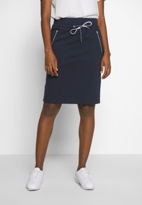 Marineblauer knielanger Rock aus weichem Material. Mit elastischem Bund und zwei seitlichen Reißverschlusstaschen. Glatte Textur und taillierte Passform.