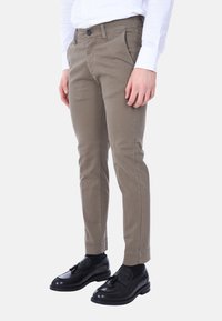 Pantaloni in cotone khaki con vestibilità slim, dotati di tasche laterali e chiusura con bottone, indossati con mocassini neri e calzini neri.