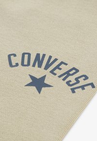 Bežna pamučna tkanina s teksturiranim tkanjem, s odvažnim plavim tekstom "CONVERSE" i emblemom zvijezde. Jednostavan dizajn, minimalističke naglaske.