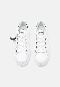 Beli usnjeni supergi s okroglo konico, črnim poudarkom na peti in šestimi luknjicami za vezalke. Imajo označen jeziček z blagovno znamko in majhno obesek v obliki risanega lika.