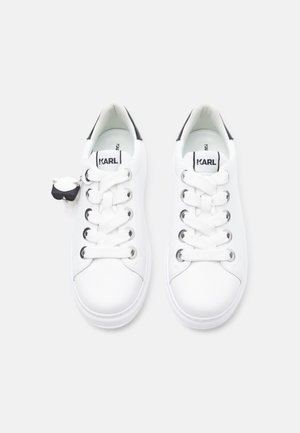 Baltas ādas sporta kurpes ar apaļu purngalu, melnu papēža akcentu un sešām acu caurumiem. Ir zīmola mēle un neliels karikatūras figūras atslēgu piekariņš.