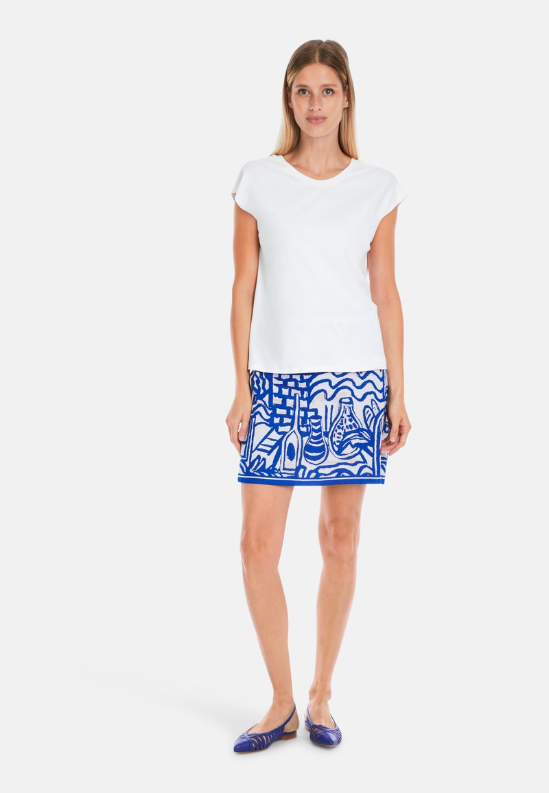 White short-sleeve top paired with a blue skirt featuring abstract patterns. The skirt has a hem accent in a darker blue tone.