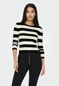 Zwart en crèmekleurig gestreepte, geribbelde trui met lange mouwen en een ronde halslijn, gecombineerd met zwarte, high-waisted jeans met knoopdetails.