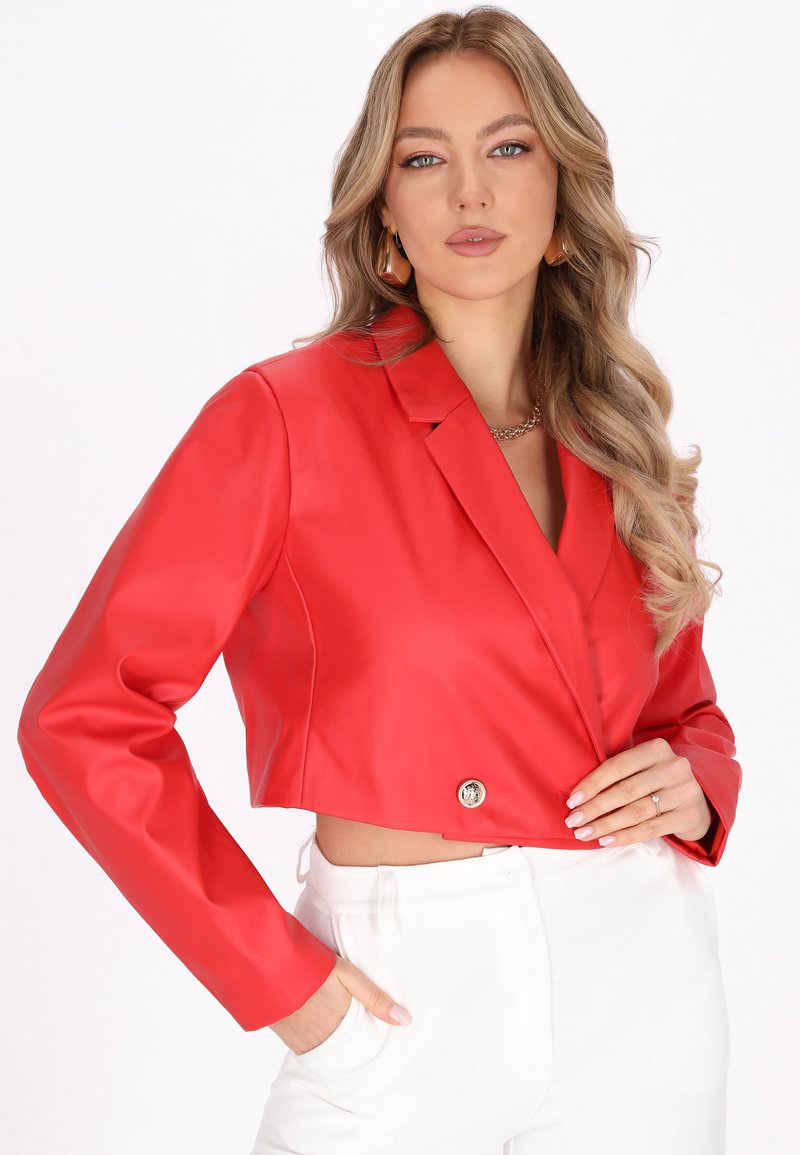 Afskåret rød faux læder blazer med et spidst revers, enkel blank knaplukning og lange ærmer. Sammen med hvide bukser.