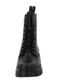 Bota de combate de cuero negro con suela gruesa, cordones delanteros y tirador en la parte superior.
