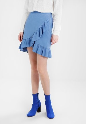 Mini jupe bleu volante en tissu doux et texturé. Présente un ourlet asymétrique et un design superposé. Associée à des bottines bleu vif.